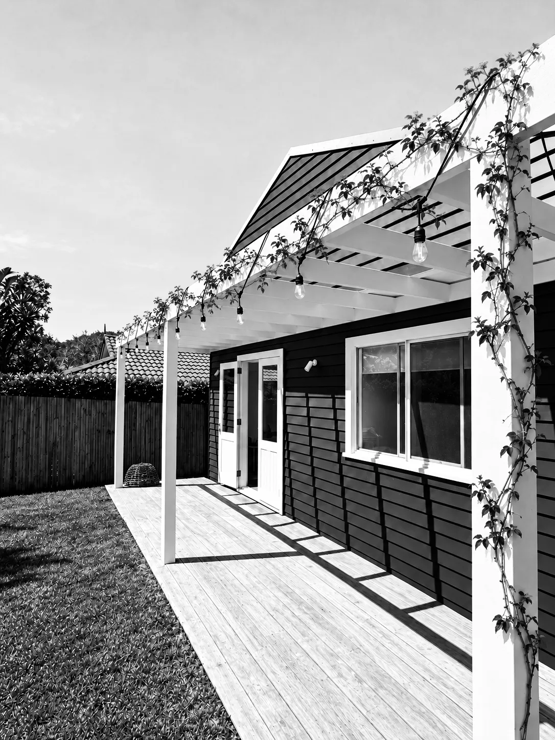 Cottage with timber deck and white pergola, black and white