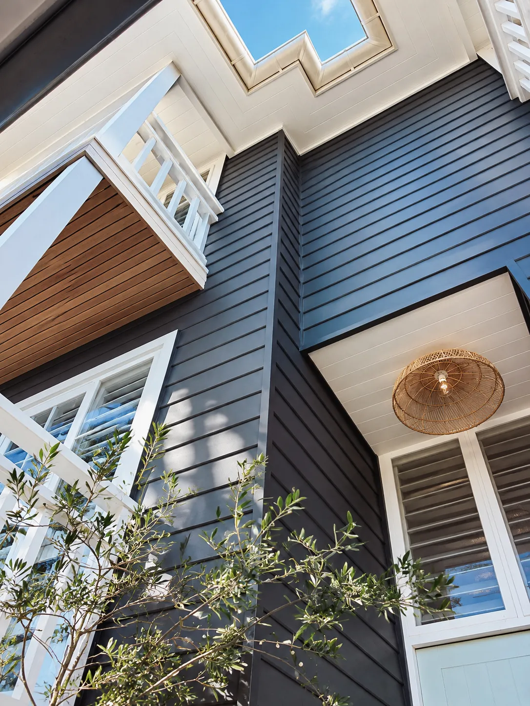 Looking up at black cladding, a timber-lined balcony and skylight