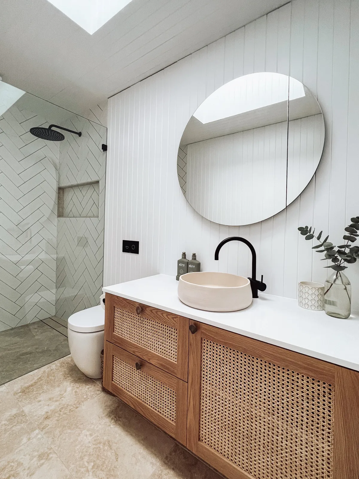Bathroom with cane-front vanity, round mirror and herringbone tiles