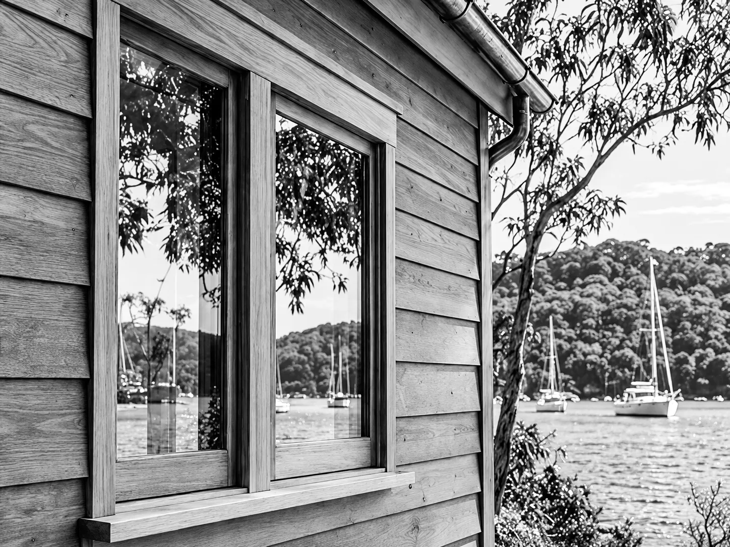Boatshed window reflecting the bay, black and white