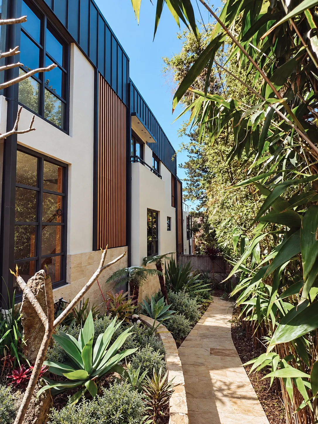 Side path past a dark-clad extension with native planting