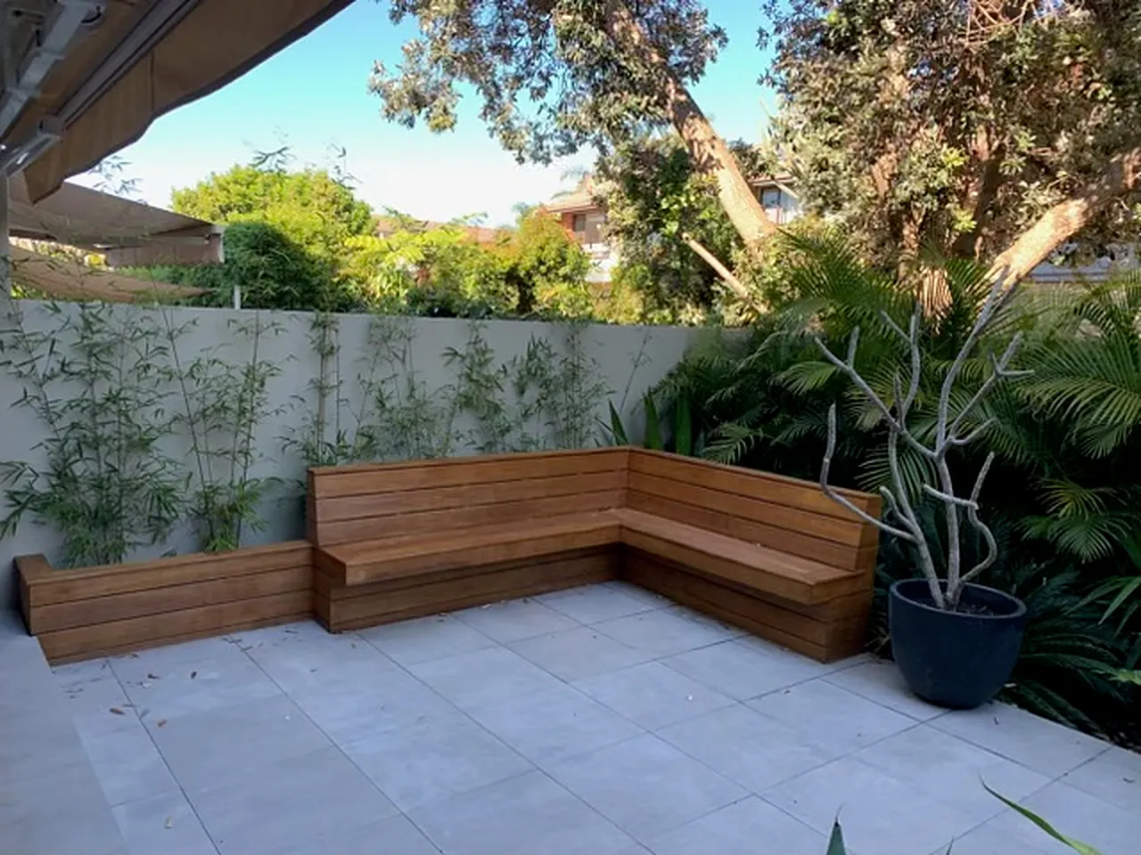 Timber corner bench and planter boxes on a pale paved courtyard